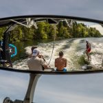 View through rear view mirror of boat of group wakesurfing on the lake on a sunny day