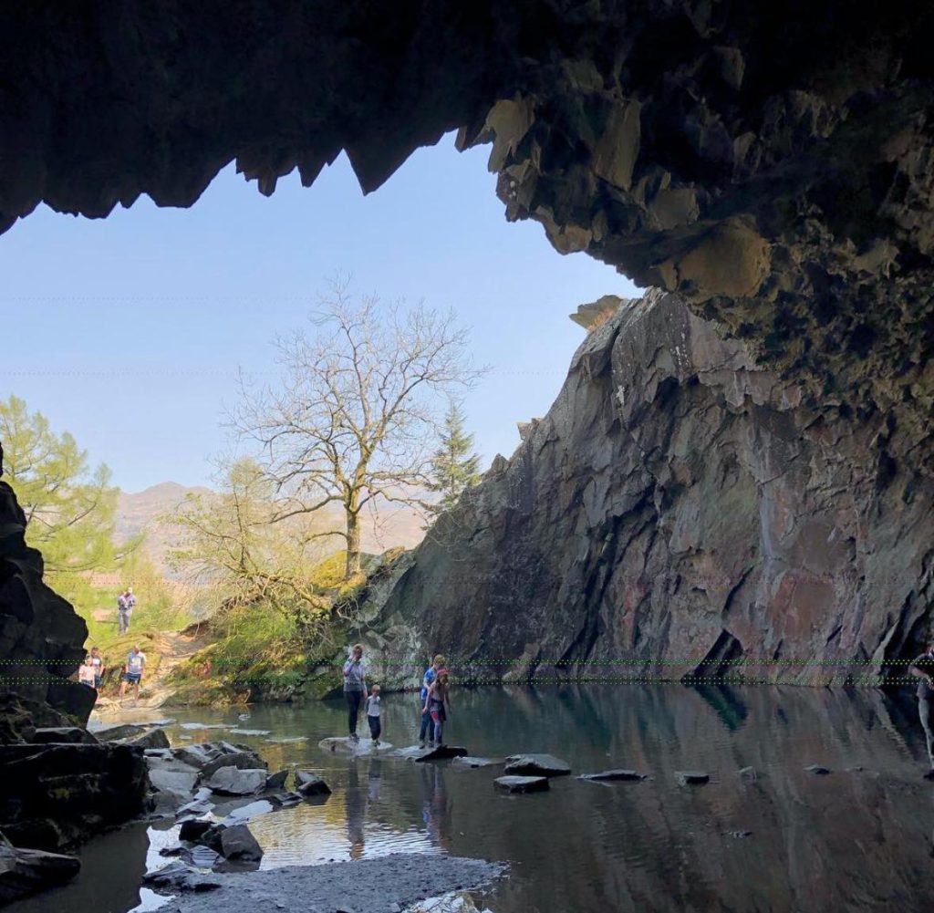 view from inside rydal cave. family walking across stepping stones in water. blue skies